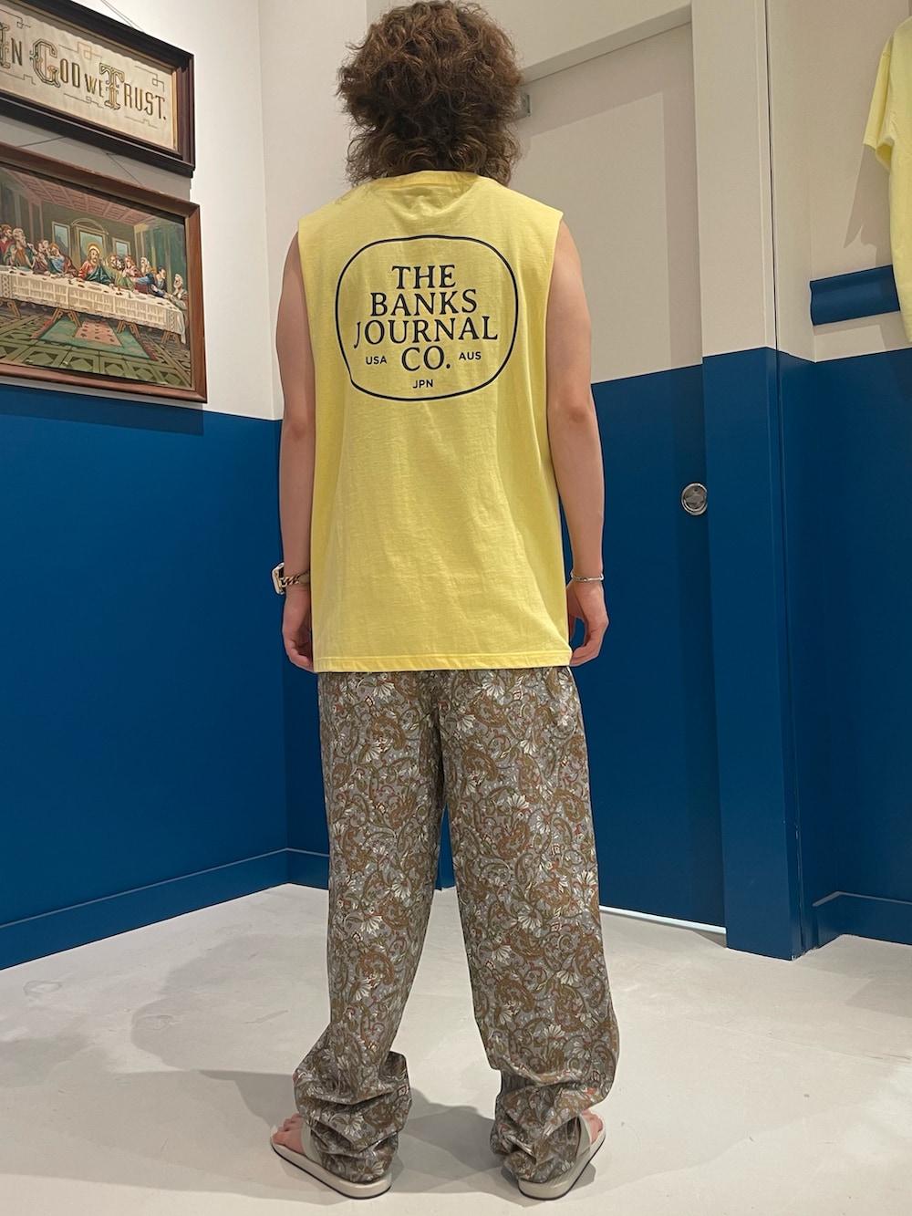イエロー系のタンクトップ、グレー系のパンツ、ホワイト系のサンダルを着用したメンズの夏コーディネートの3枚目の写真