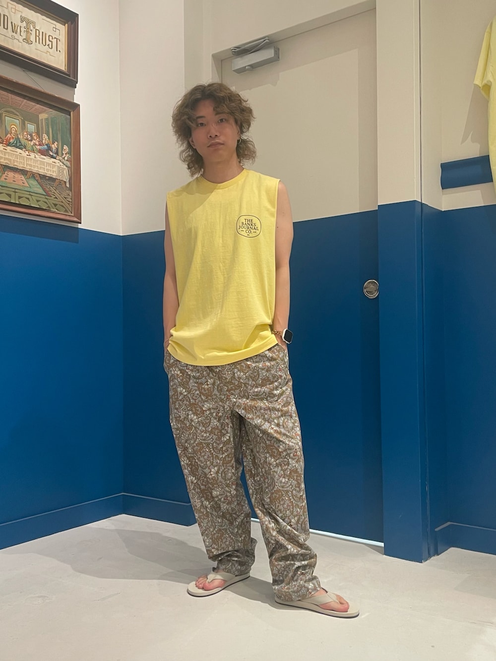 イエロー系のタンクトップ、グレー系のパンツ、ホワイト系のサンダルを着用したメンズの夏コーディネートの2枚目の写真