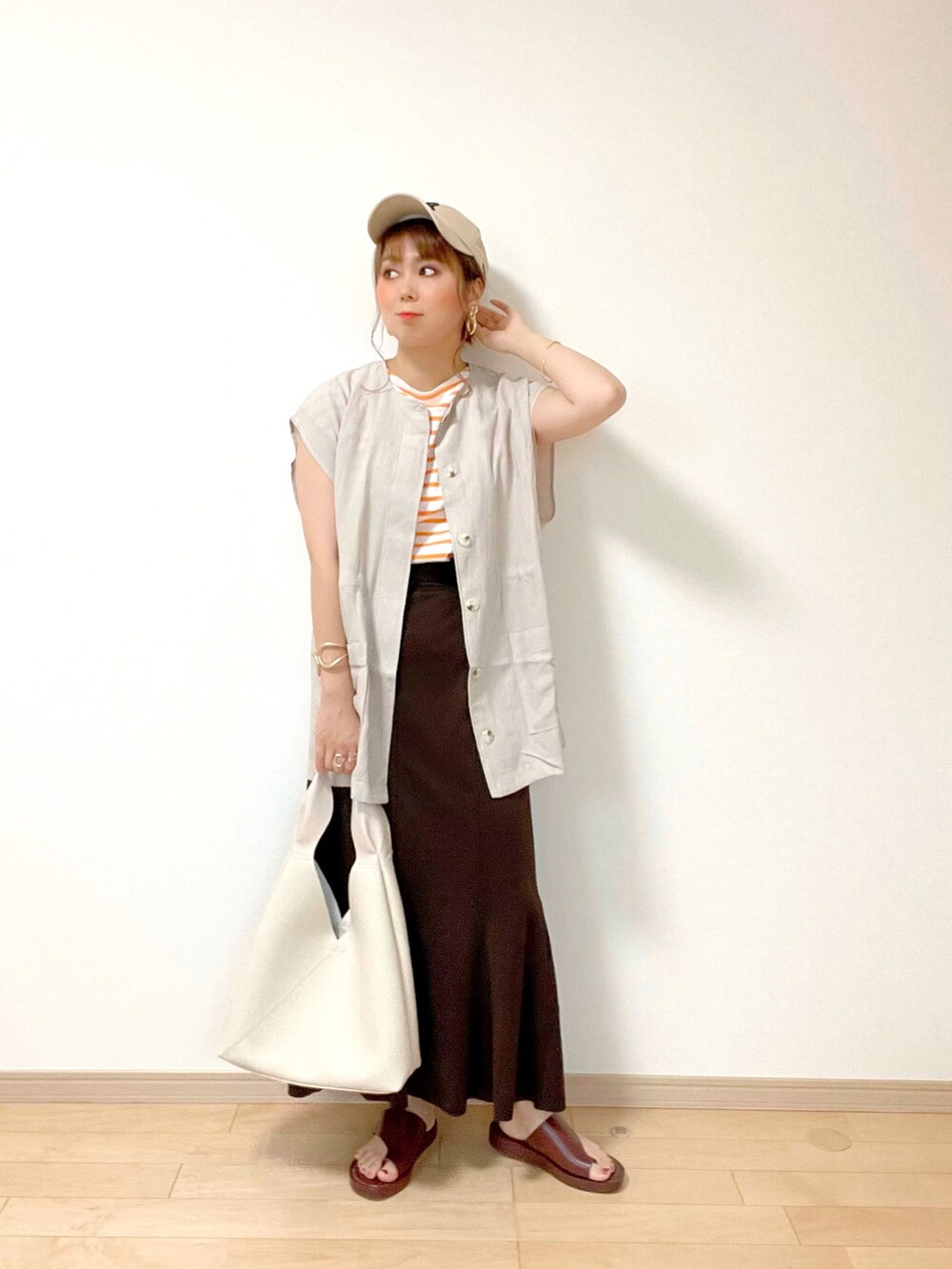 グレー系のベスト、オレンジ系のTシャツ/カットソー、ブラウン系のスカートを着用したレディースの夏コーディネートの2枚目の写真