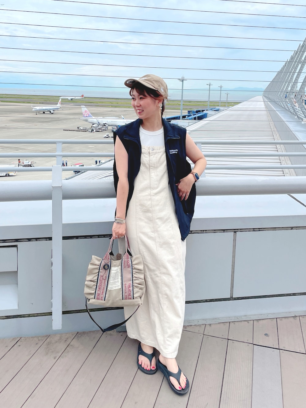 ブラック系のベスト、ホワイト系のタンクトップ、ベージュ系のジャンパースカートを着用したレディースの夏コーディネートの2枚目の写真