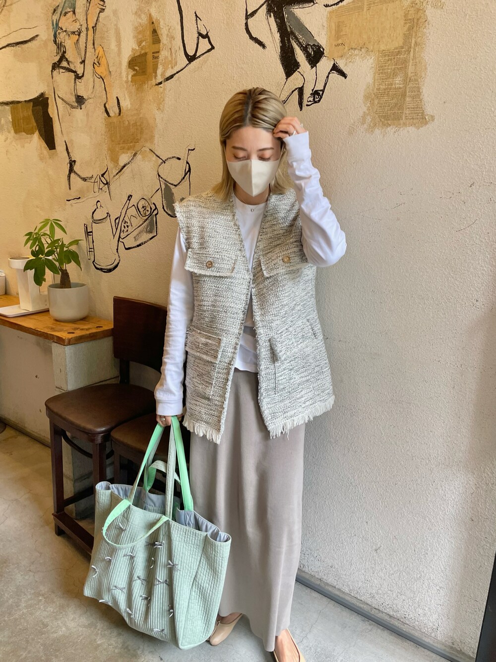グレー系のベスト、グリーン系のトートバッグ、グレー系のスカートを着用したレディースの春コーディネートの3枚目の写真