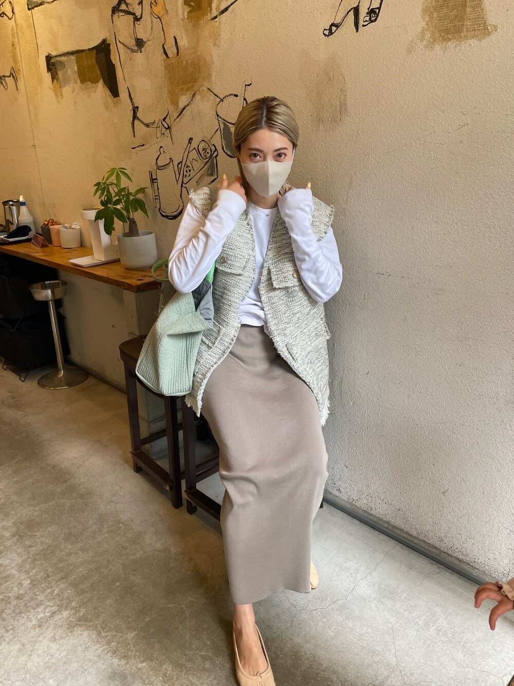 グレー系のベスト、グリーン系のトートバッグ、グレー系のスカートを着用したレディースの春コーディネートの2枚目の写真