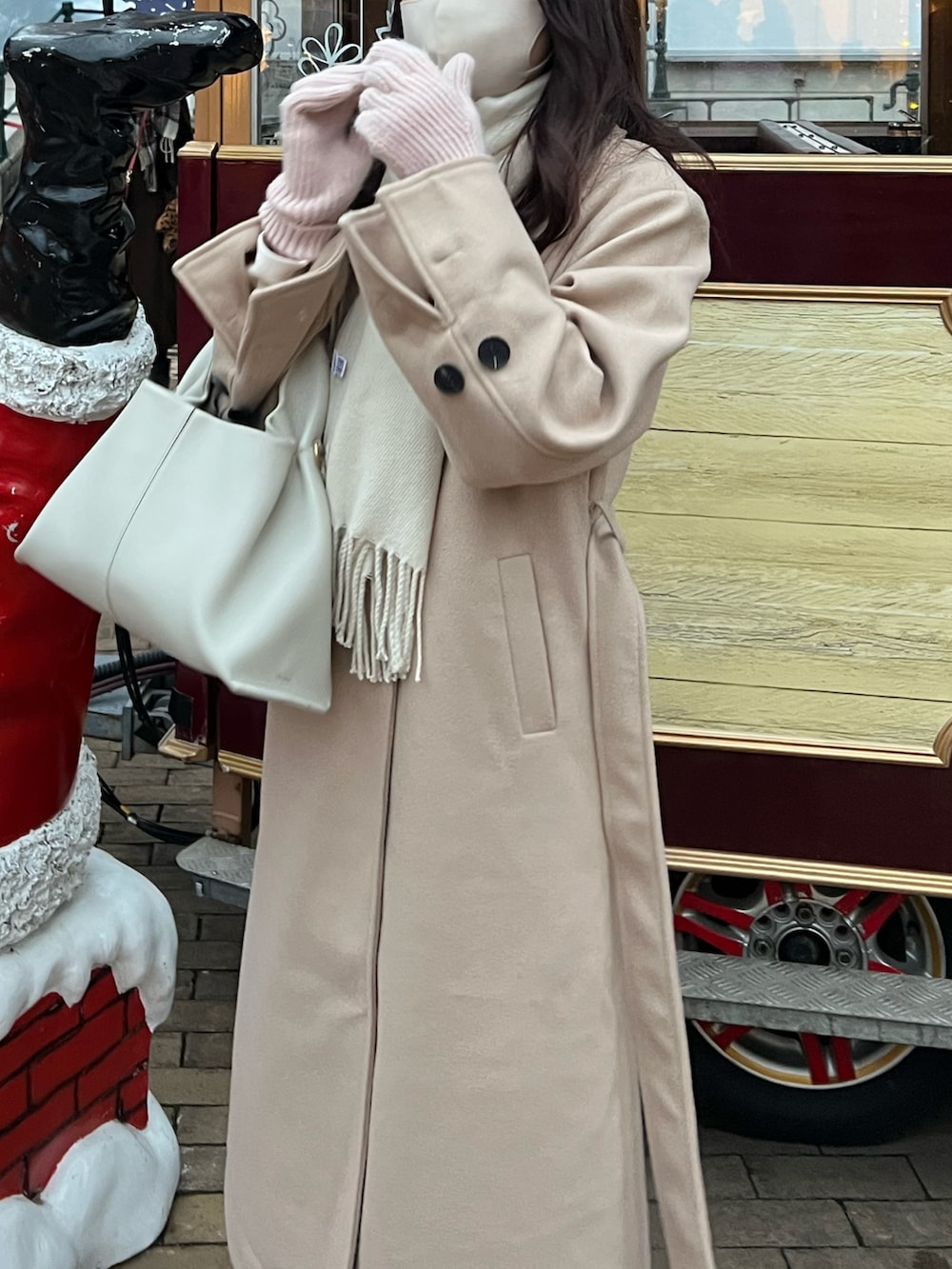 ベージュ系のチェスターコート、ホワイト系のハンドバッグ、ベージュ系のブーツを着用したレディースの冬コーディネートの2枚目の写真