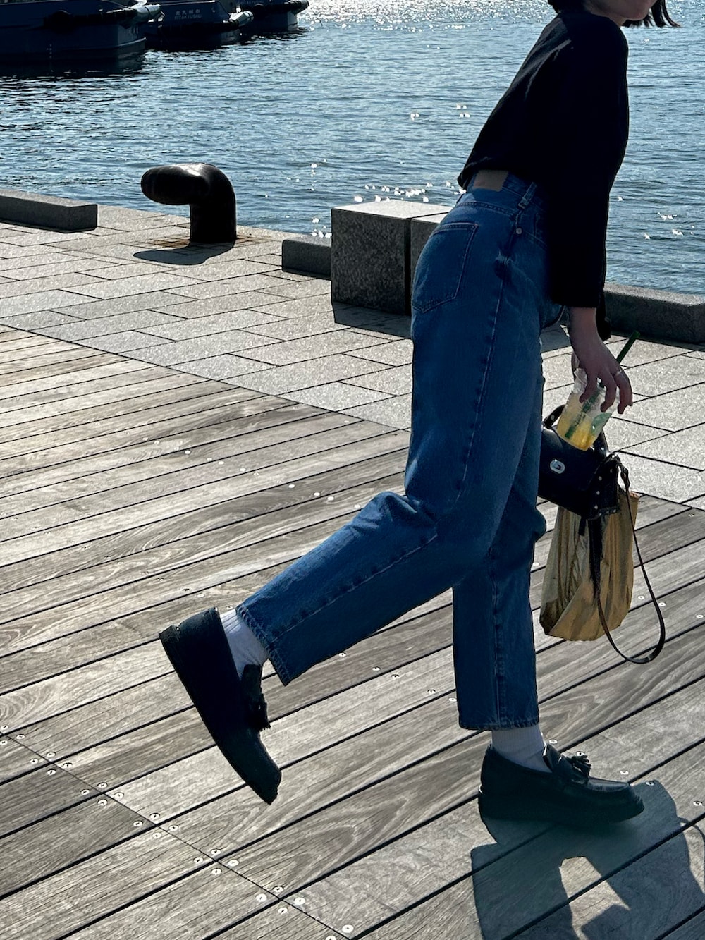 ブラック系のTシャツ/カットソー、ブルー系のデニムパンツ、ブラック系のショルダーバッグを着用したレディースの春コーディネートの4枚目の写真