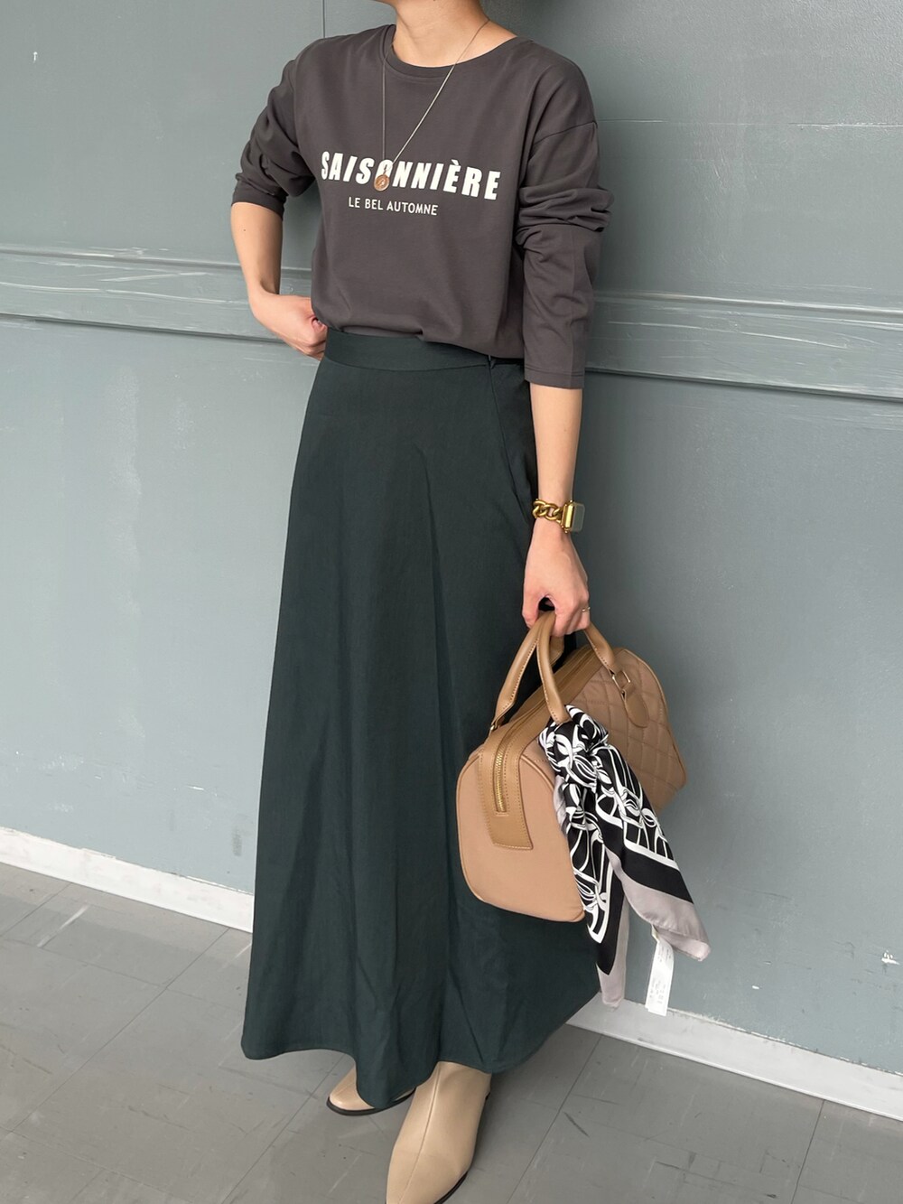 ベージュ系のハンドバッグ、グレー系のTシャツ/カットソー、グリーン系のスカートを着用したレディースの秋コーディネートの2枚目の写真