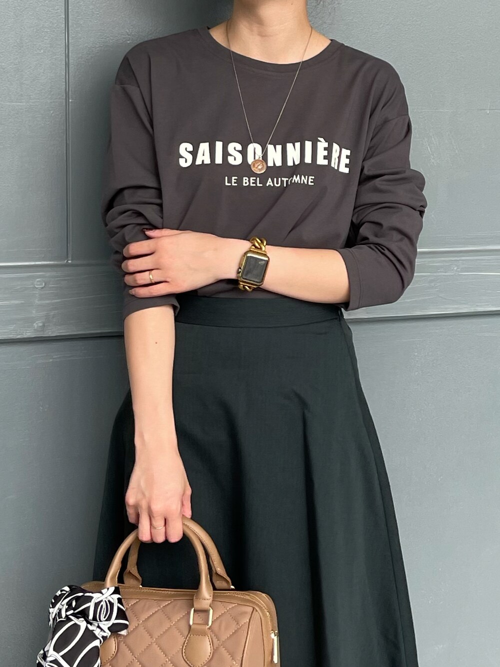 ベージュ系のハンドバッグ、グレー系のTシャツ/カットソー、グリーン系のスカートを着用したレディースの秋コーディネートの3枚目の写真