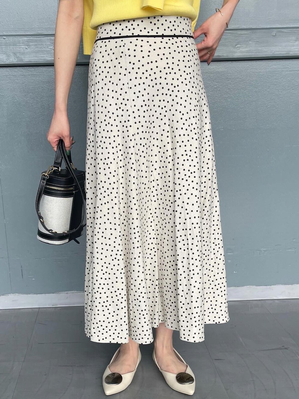 イエロー系のニット/セーター、ホワイト系のスカート、ブラック系のショルダーバッグを着用したレディースの春コーディネートの3枚目の写真