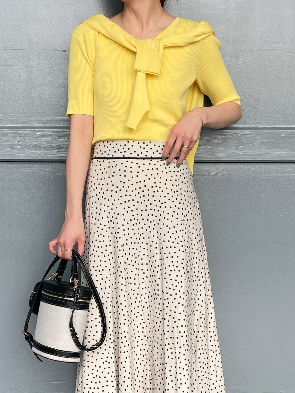 イエロー系のニット/セーター、ホワイト系のスカート、ブラック系のショルダーバッグを着用したレディースの春コーディネートの2枚目の写真