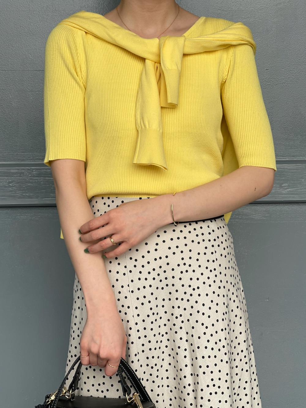 イエロー系のニット/セーター、ホワイト系のスカート、ブラック系のショルダーバッグを着用したレディースの春コーディネートの4枚目の写真