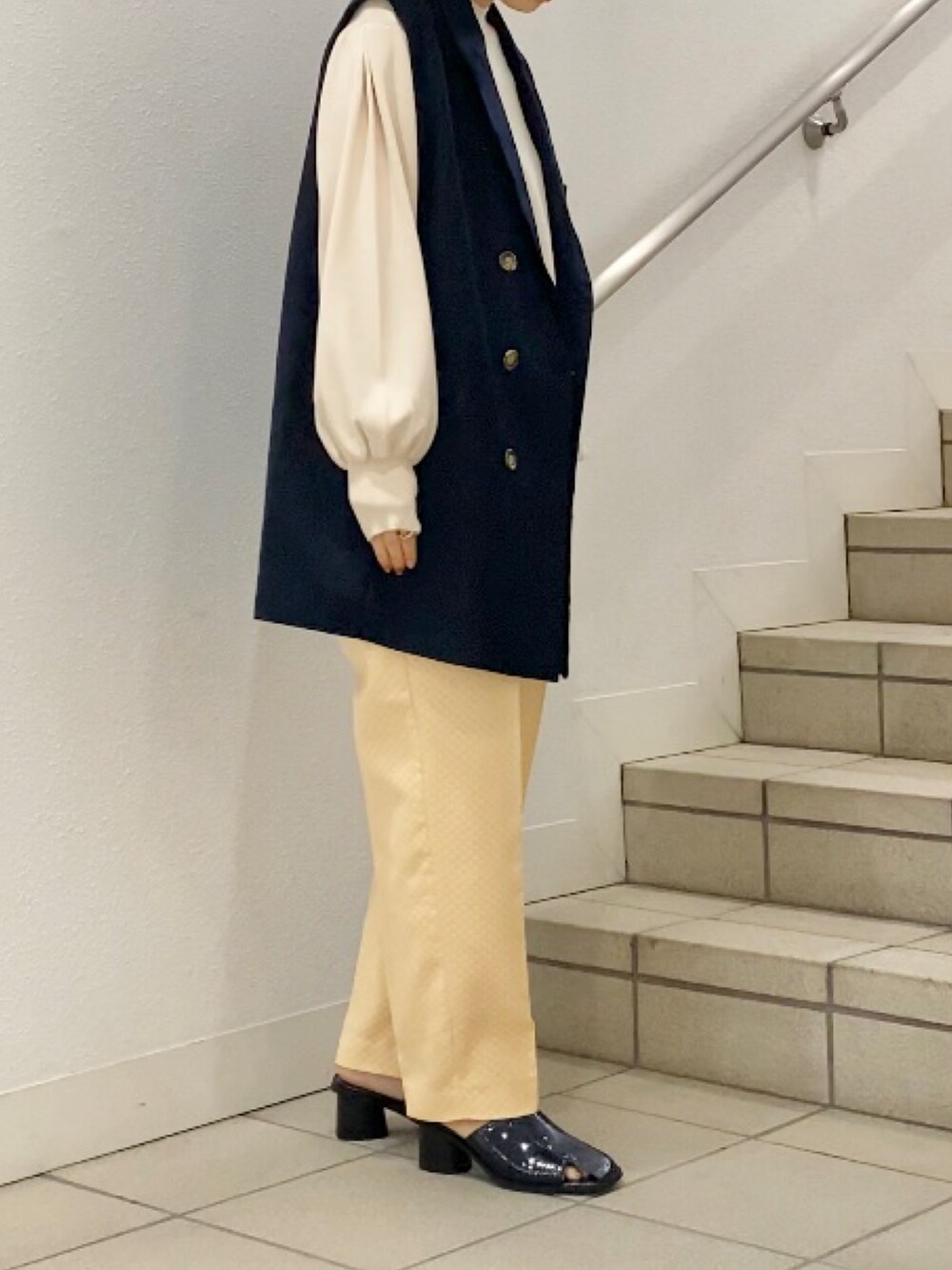 イエロー系のサンダル、イエロー系のその他パンツ、ブルー系のベストを着用したレディースの春コーディネートの3枚目の写真