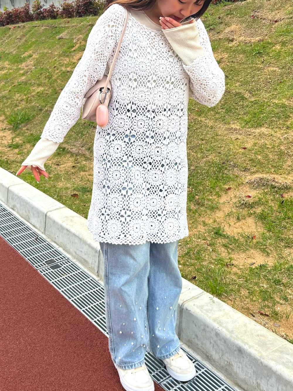 ブルー系のデニムパンツ、ベージュ系のハンドバッグ、ホワイト系のニット/セーターを着用したレディースの春コーディネートの3枚目の写真