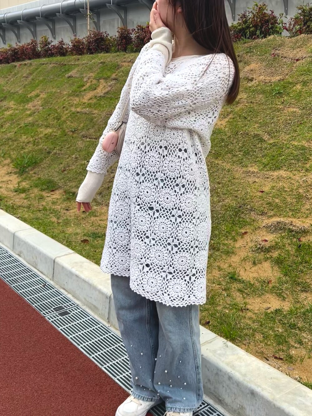ブルー系のデニムパンツ、ベージュ系のハンドバッグ、ホワイト系のニット/セーターを着用したレディースの春コーディネートの4枚目の写真