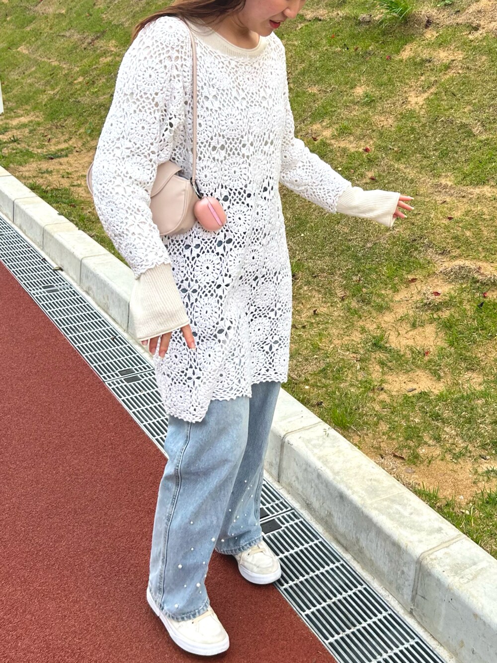 ブルー系のデニムパンツ、ベージュ系のハンドバッグ、ホワイト系のニット/セーターを着用したレディースの春コーディネートの2枚目の写真