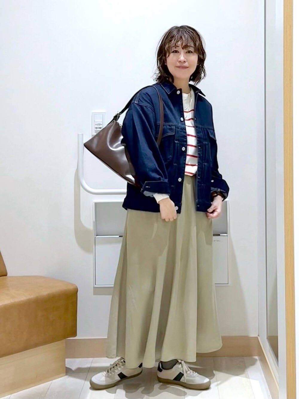 ベージュ系のスニーカー、ブラウン系のショルダーバッグ、ブルー系のデニムジャケットを着用したレディースの春コーディネートの2枚目の写真