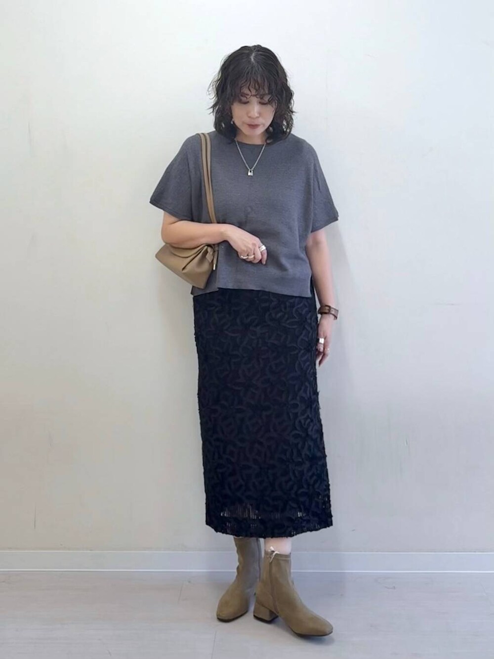 グレー系のニット/セーター、ベージュ系のショルダーバッグ、ブラック系のスカートを着用したレディースの夏コーディネートの2枚目の写真