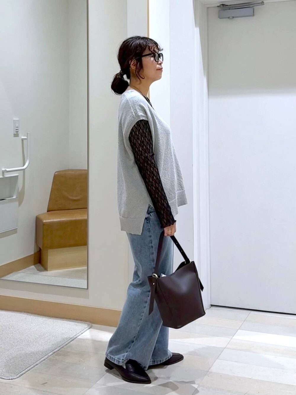 ブラウン系のショルダーバッグ、ブルー系のデニムパンツ、グレー系のベストを着用したレディースの秋コーディネートの3枚目の写真
