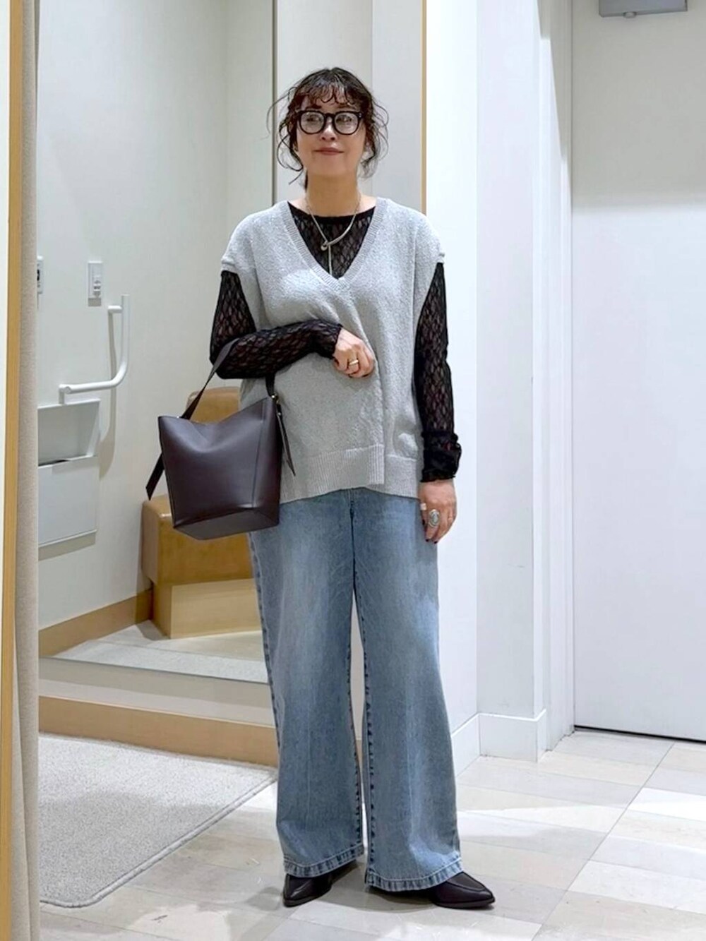 ブラウン系のショルダーバッグ、ブルー系のデニムパンツ、グレー系のベストを着用したレディースの秋コーディネートの2枚目の写真
