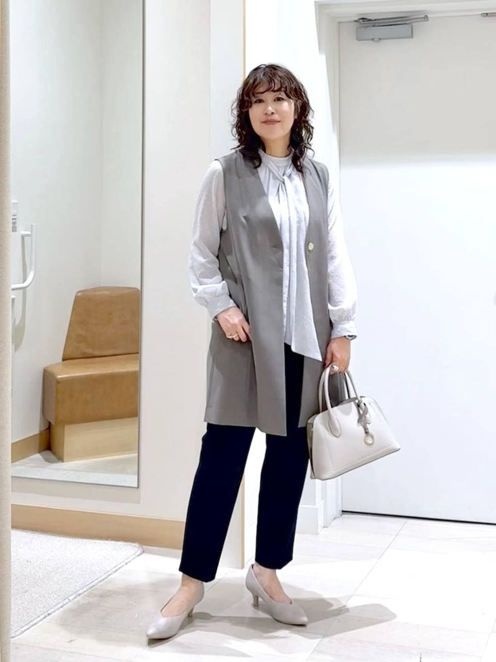 ホワイト系のショルダーバッグ、ホワイト系のパンプス、ブルー系のスラックスを着用したレディースの春コーディネートの2枚目の写真