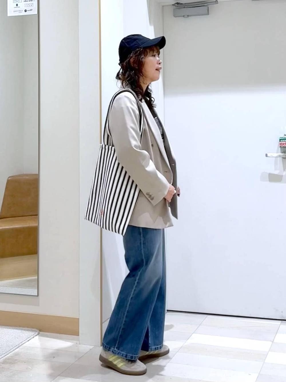 ブルー系のデニムパンツ、ベージュ系のテーラードジャケット、ホワイト系のトートバッグを着用したレディースの春コーディネートの3枚目の写真