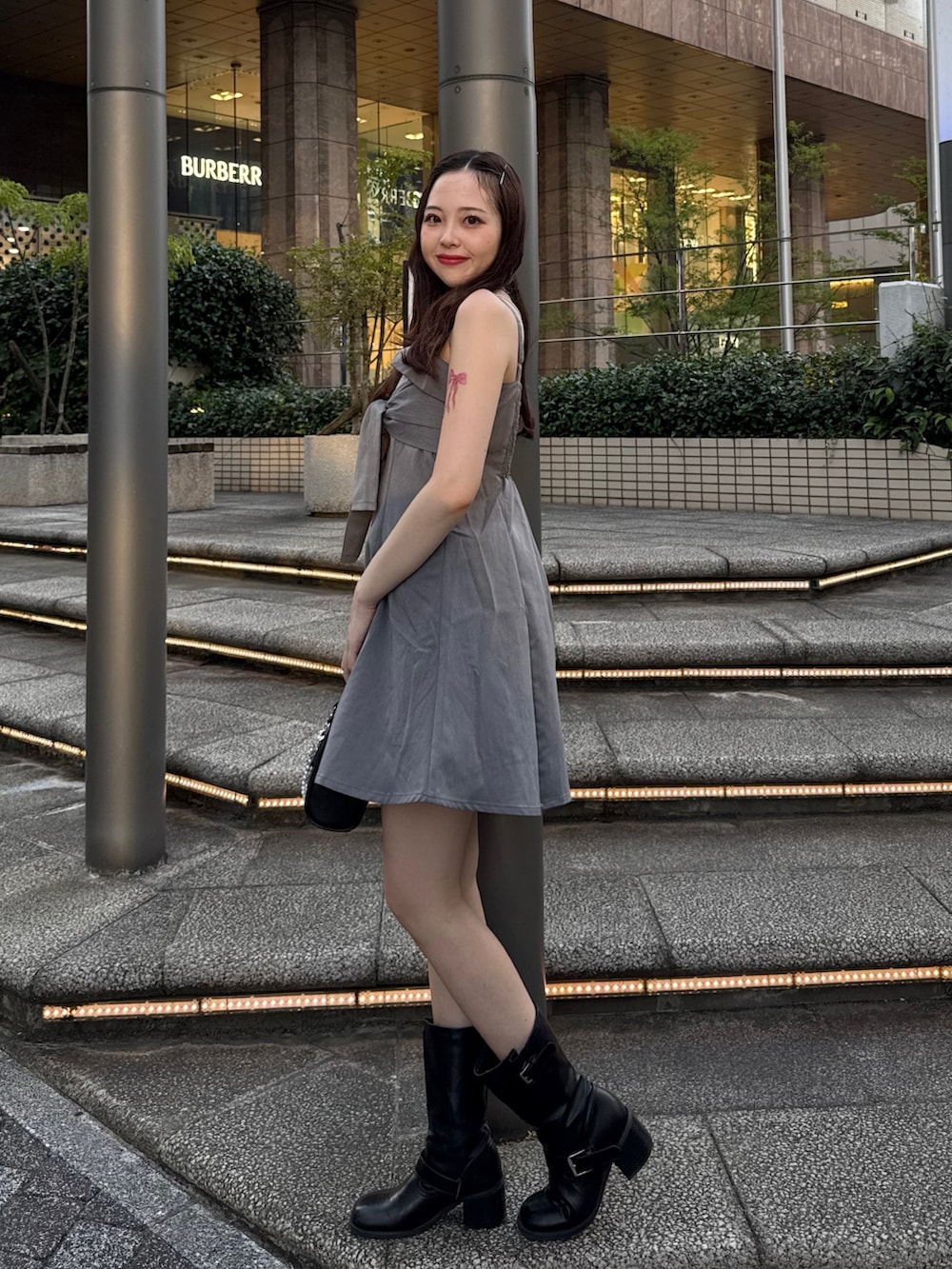 グレー系のワンピース、ブラック系のボストンバッグ、ブラック系のブーツを着用したレディースの夏コーディネートの2枚目の写真