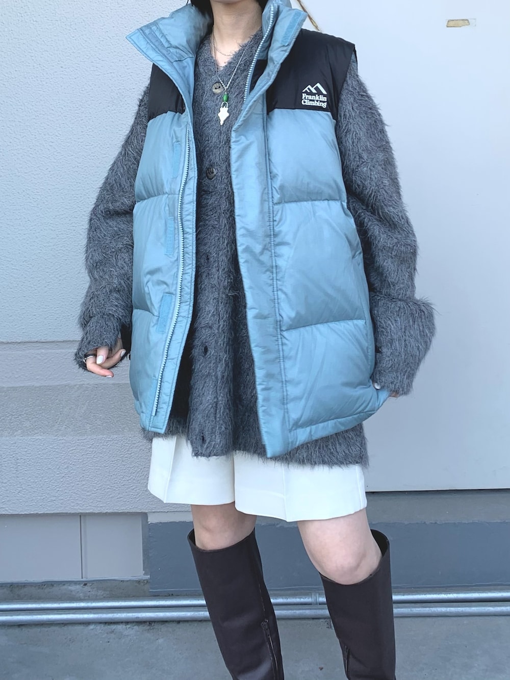 グレー系のニット/セーター、ブルー系のダウンベスト、ブラウン系のブーツを着用したレディースの秋コーディネートの3枚目の写真