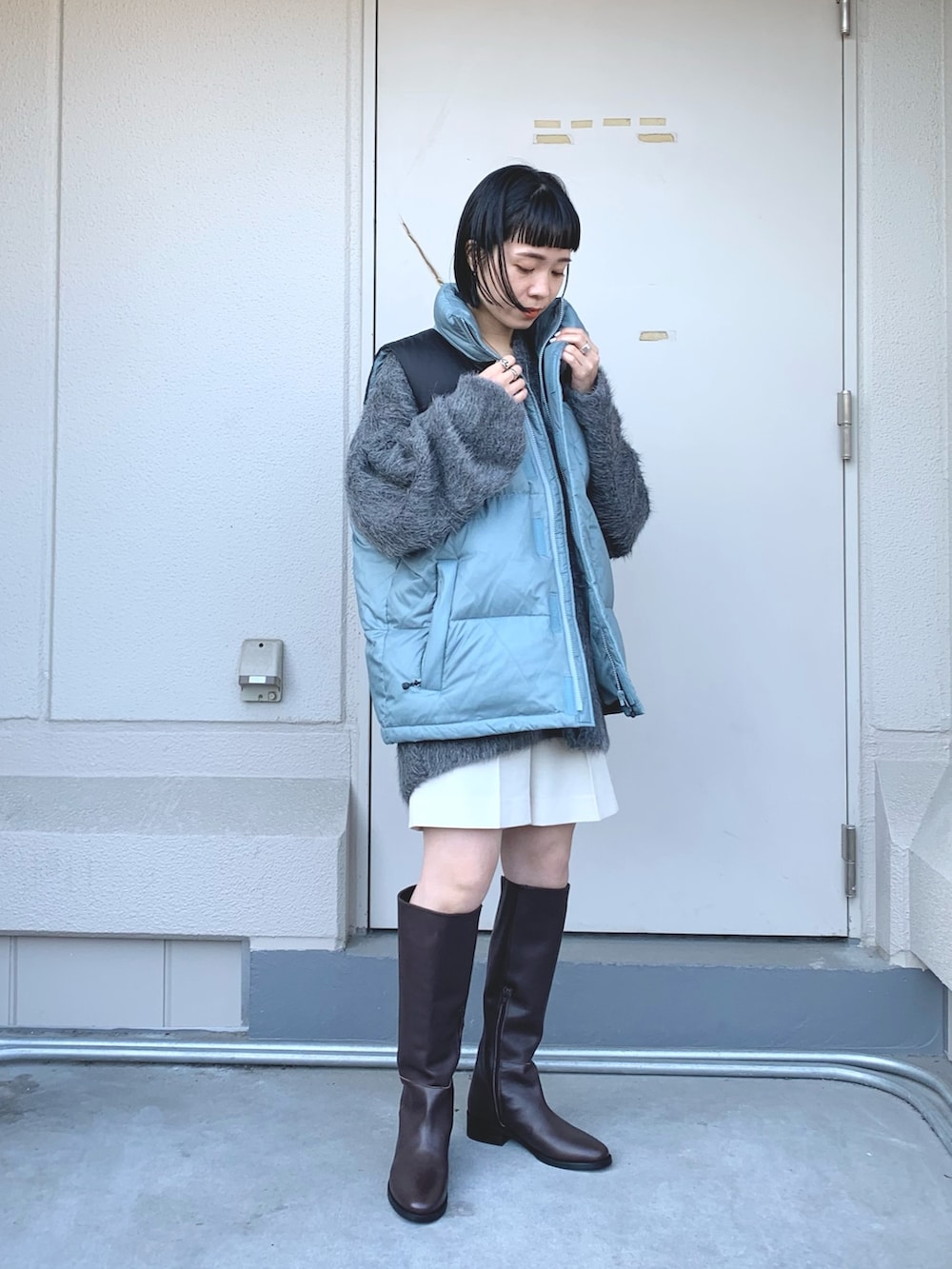 グレー系のニット/セーター、ブルー系のダウンベスト、ブラウン系のブーツを着用したレディースの秋コーディネートの2枚目の写真