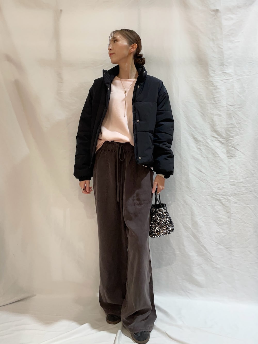 ピンク系のニット/セーター、ブラック系のダウンジャケット/コート、シルバー系のショルダーバッグを着用したレディースの秋コーディネートの2枚目の写真