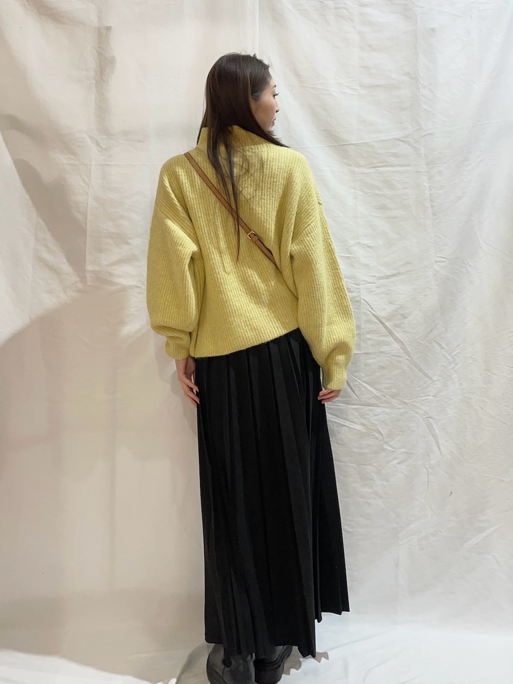 ブラック系のスカート、ブラック系のショルダーバッグ、イエロー系のニット/セーターを着用したレディースの冬コーディネートの2枚目の写真