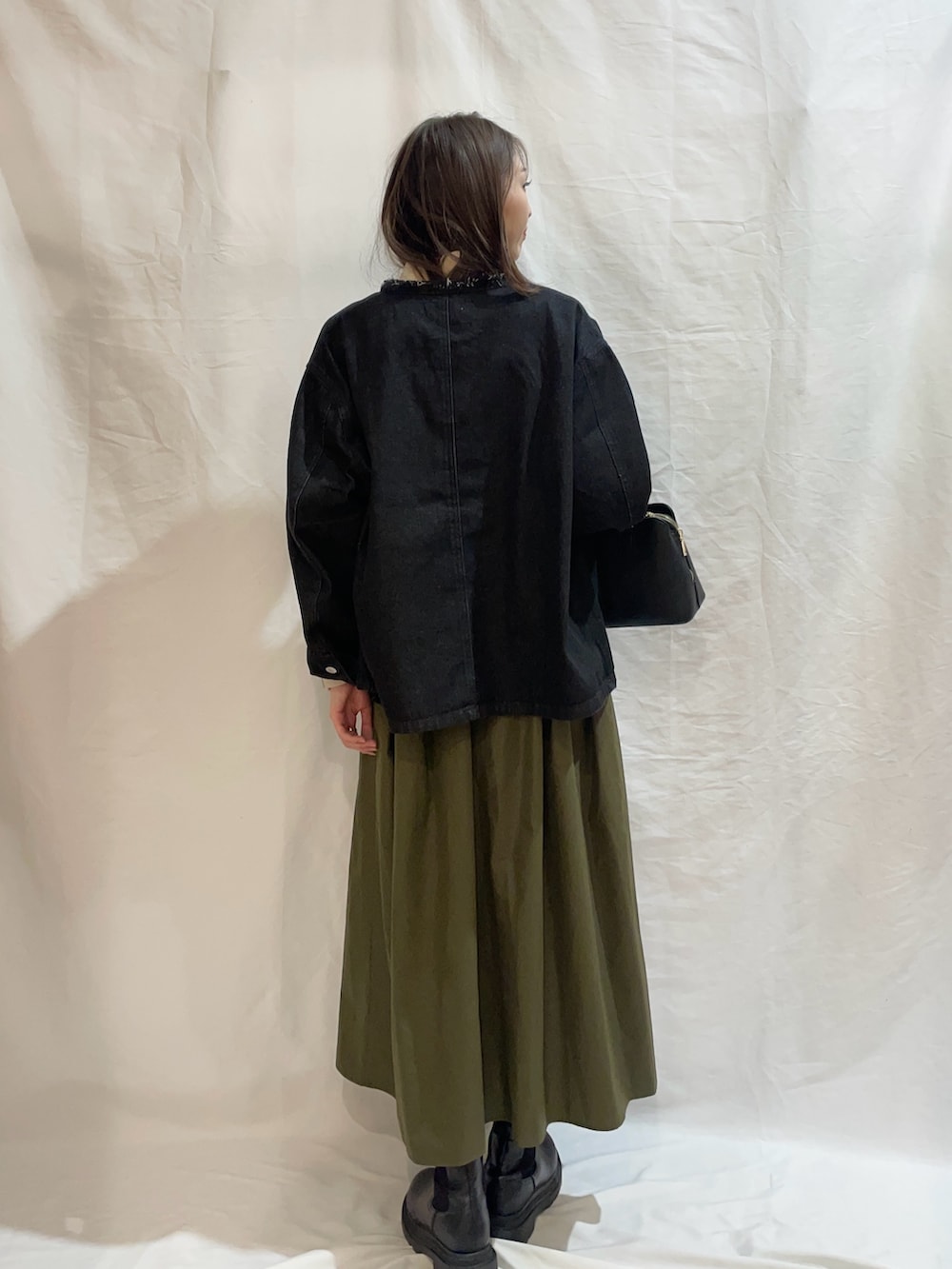 グリーン系のスカート、ブラック系のデニムジャケット、ホワイト系のニット/セーターを着用したレディースの冬コーディネートの3枚目の写真