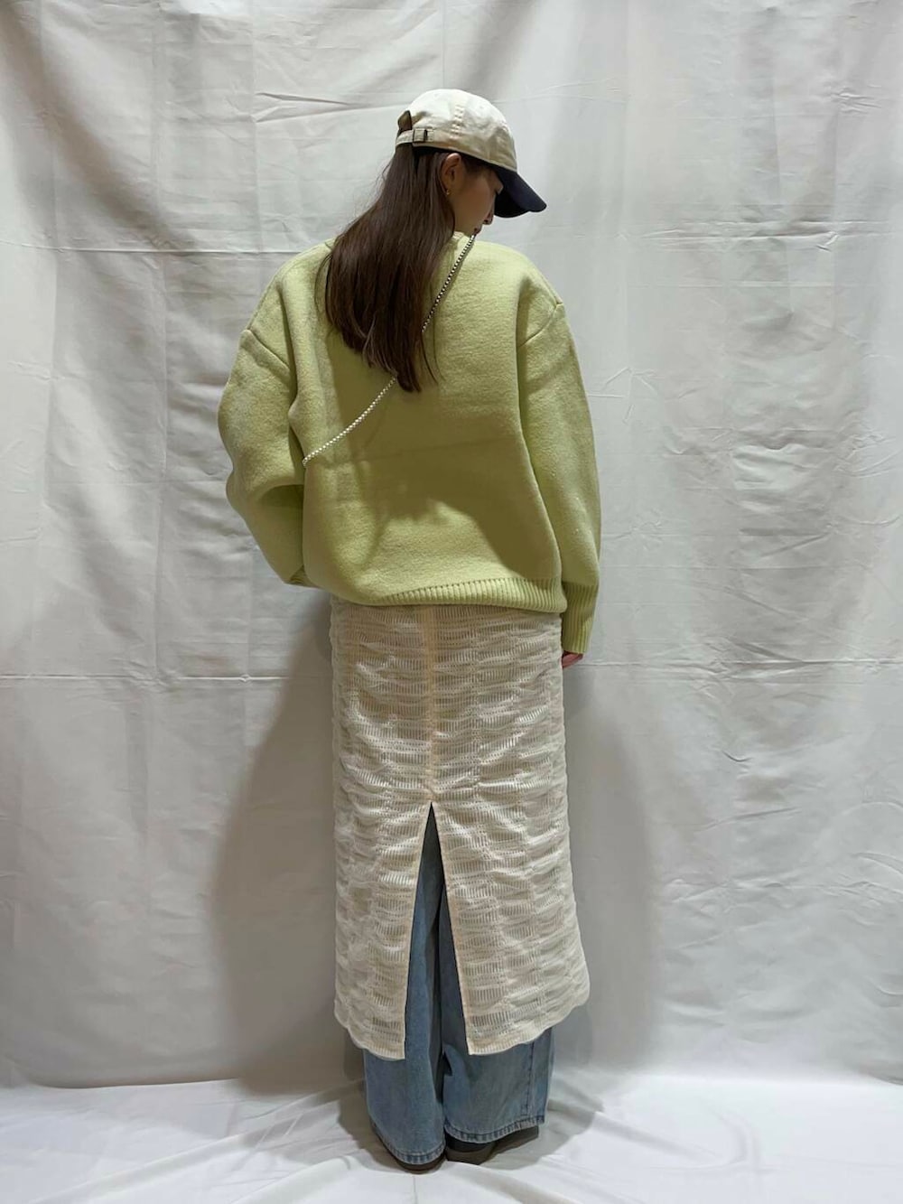 ブルー系のデニムパンツ、ホワイト系のスカート、グリーン系のニット/セーターを着用したレディースの冬コーディネートの2枚目の写真