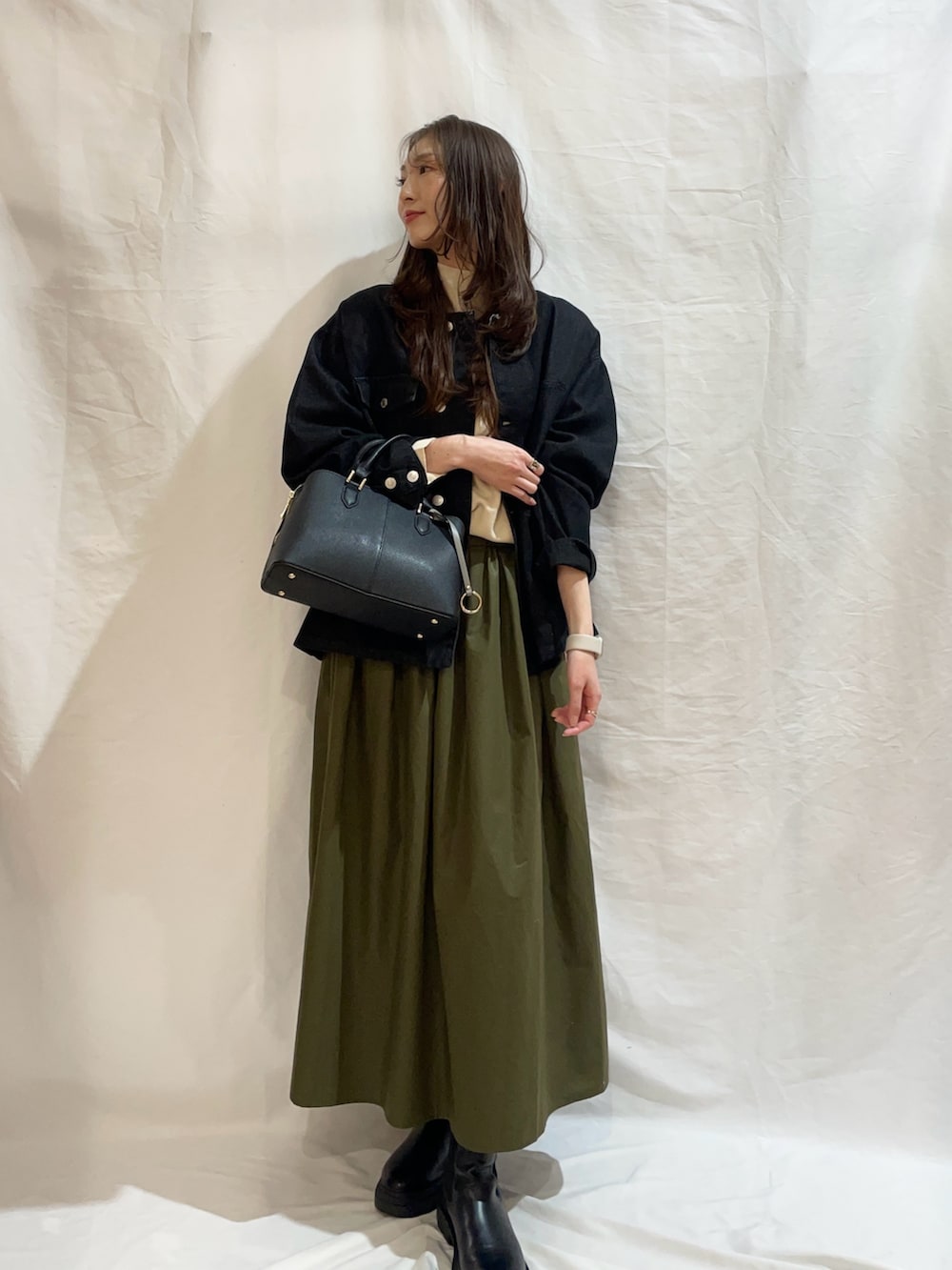 グリーン系のスカート、ブラック系のデニムジャケット、ホワイト系のニット/セーターを着用したレディースの冬コーディネートの2枚目の写真