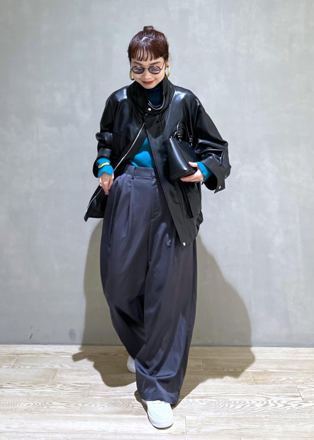 ブラック系のハンドバッグ、ブラック系のライダースジャケット、ブルー系のニット/セーターを着用したレディースの秋コーディネートの3枚目の写真