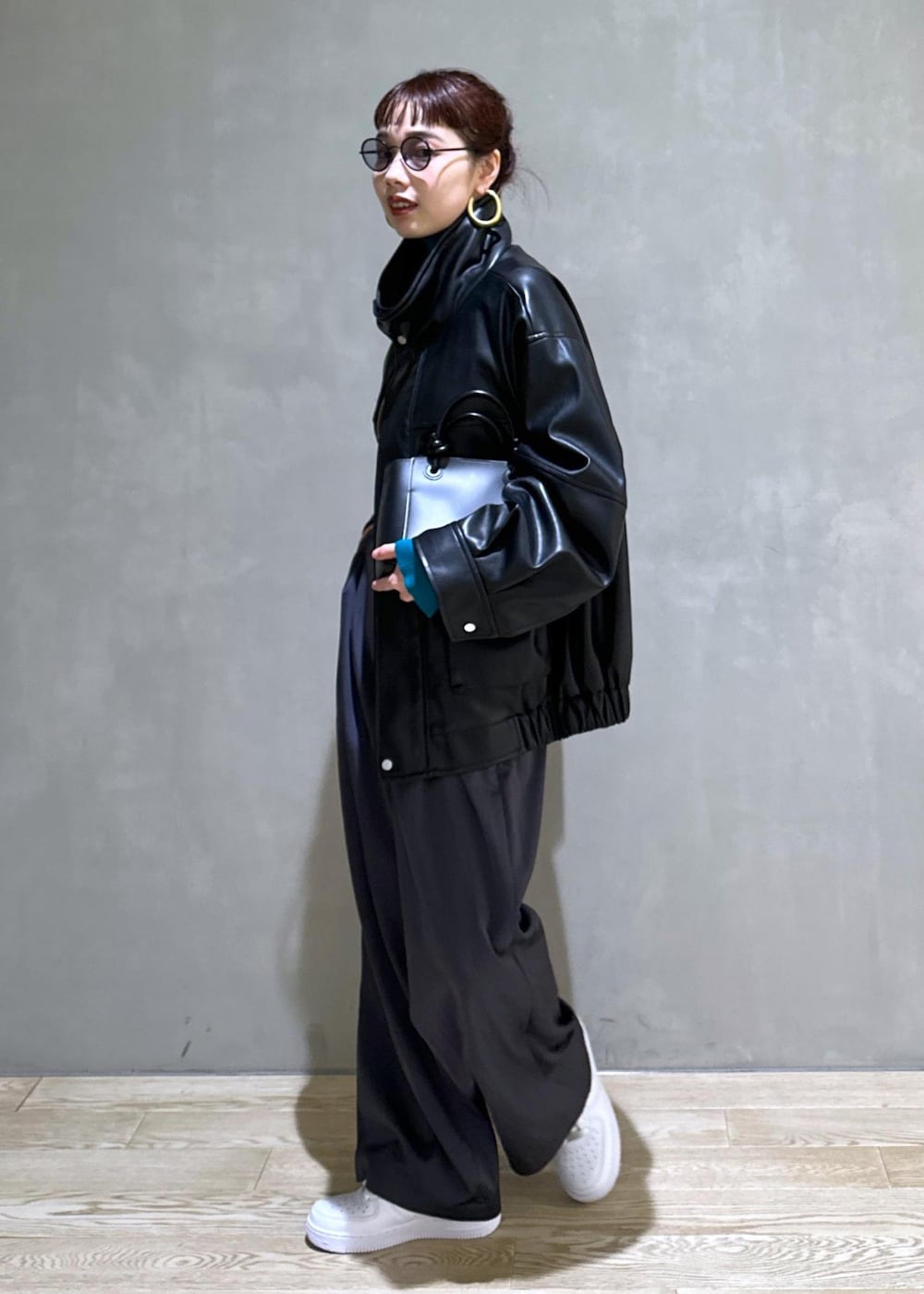 ブラック系のハンドバッグ、ブラック系のライダースジャケット、ブルー系のニット/セーターを着用したレディースの秋コーディネートの2枚目の写真