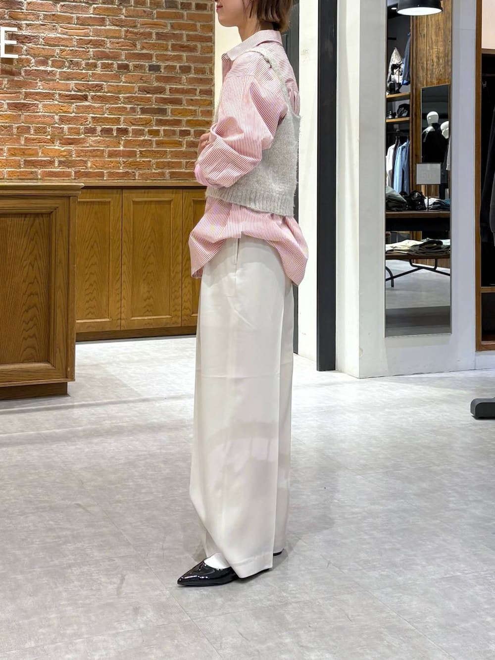 グレー系のニット/セーター、ブラック系のパンプス、ピンク系のシャツ/ブラウスを着用したレディースの春コーディネートの2枚目の写真