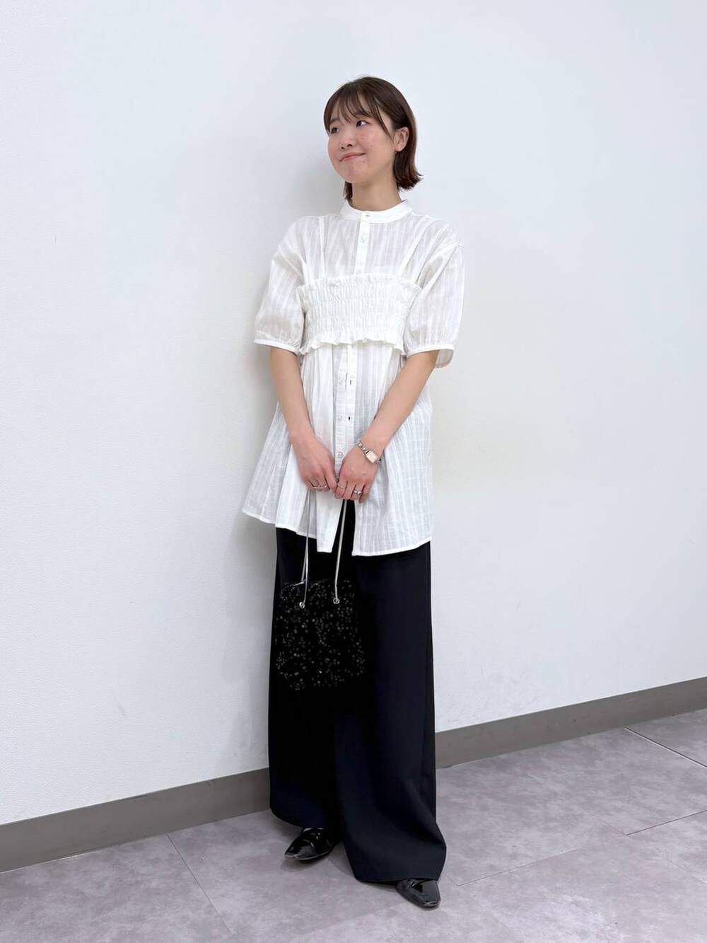 ブラック系のスラックス、ホワイト系のシャツ/ブラウス、ブラック系のハンドバッグを着用したレディースの春コーディネートの2枚目の写真