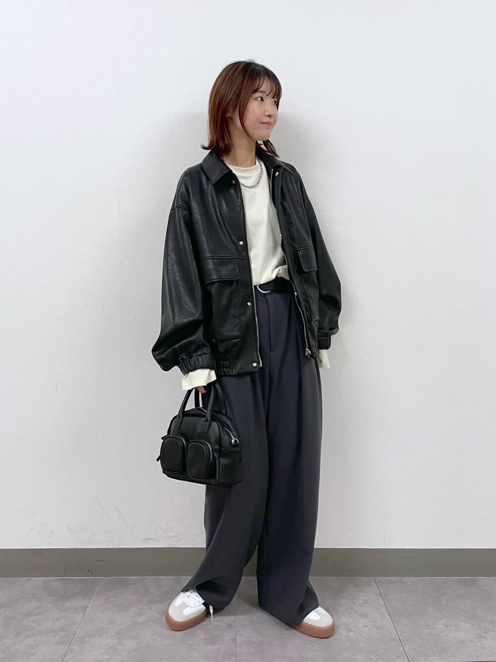 ブラック系のブルゾン、ブラック系のショルダーバッグ、グレー系のスラックスを着用したレディースの秋コーディネートの2枚目の写真