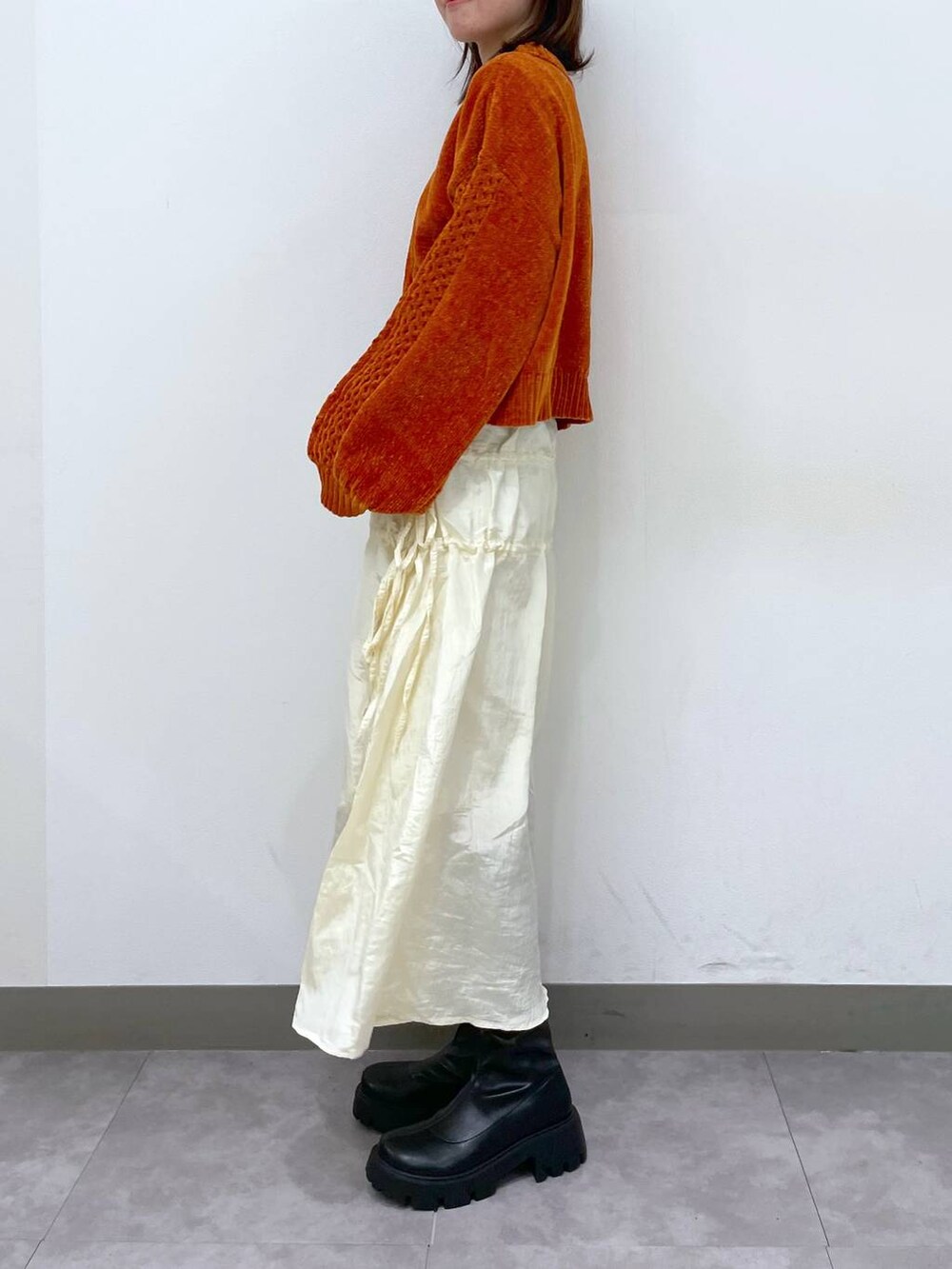 オレンジ系のニット/セーター、ブラック系のブーツ、ホワイト系のスカートを着用したレディースの秋コーディネートの2枚目の写真