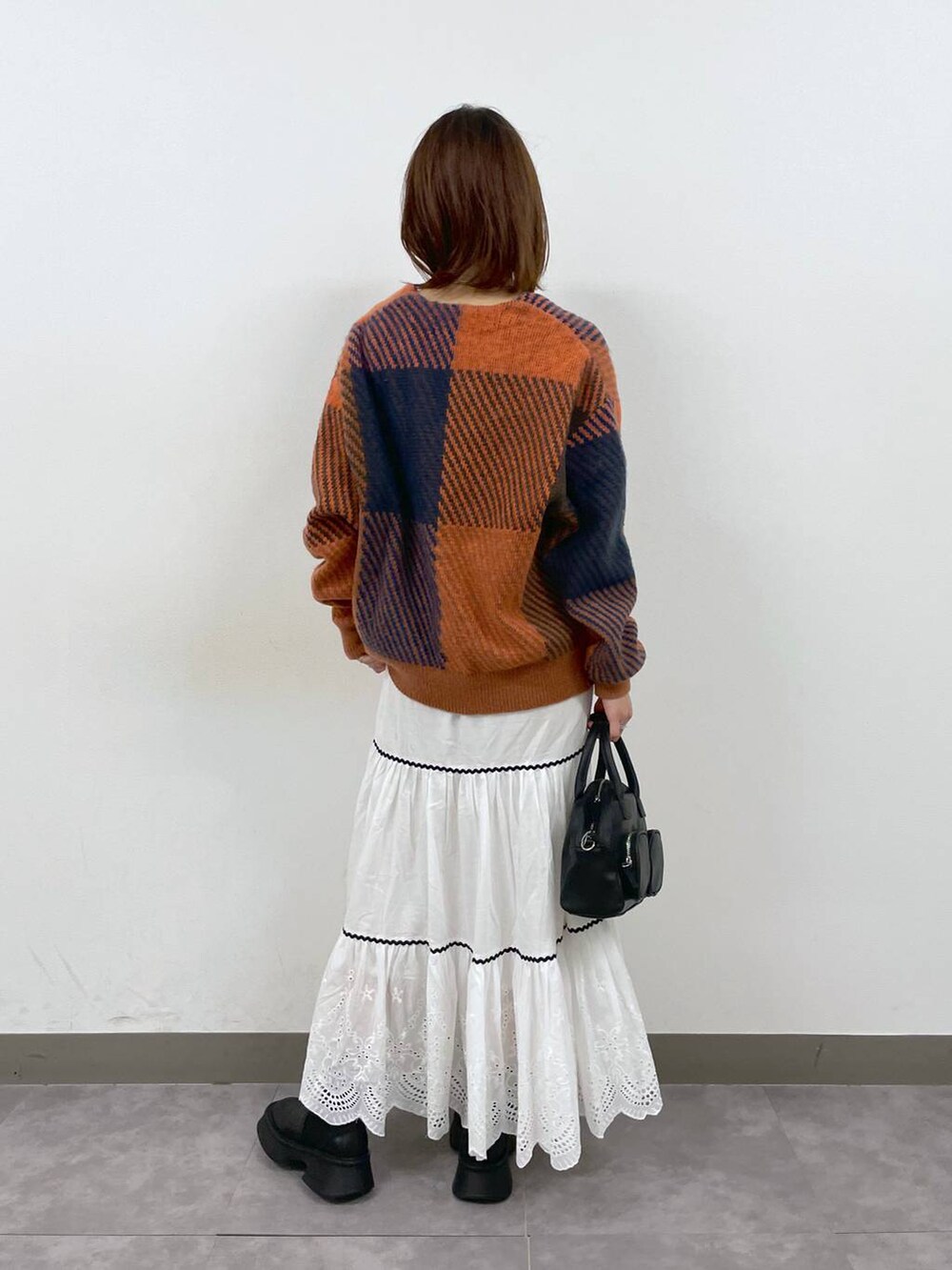 ブラック系のブーツ、ホワイト系のスカート、ブラック系のショルダーバッグを着用したレディースの秋コーディネートの4枚目の写真