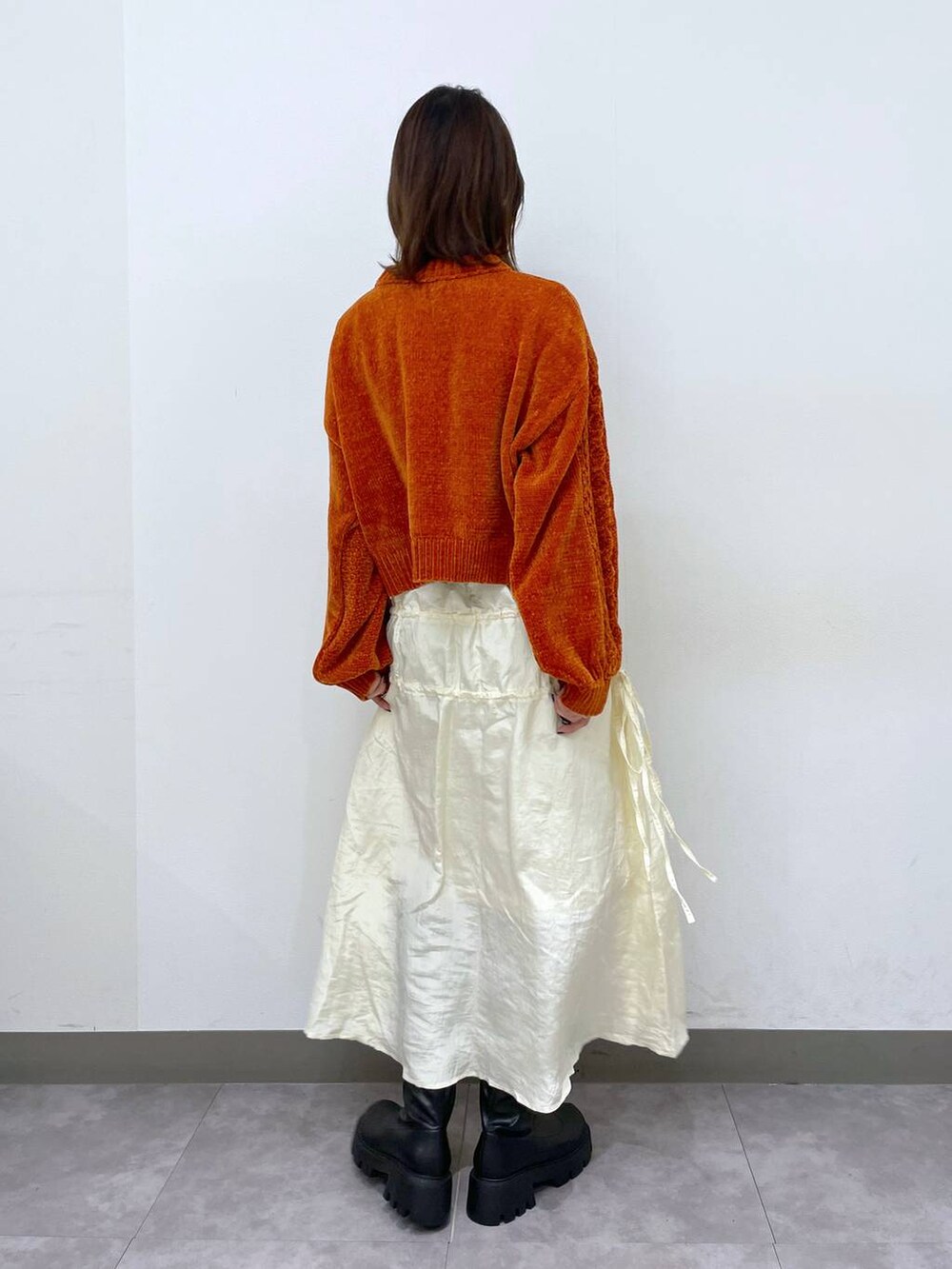 オレンジ系のニット/セーター、ブラック系のブーツ、ホワイト系のスカートを着用したレディースの秋コーディネートの4枚目の写真