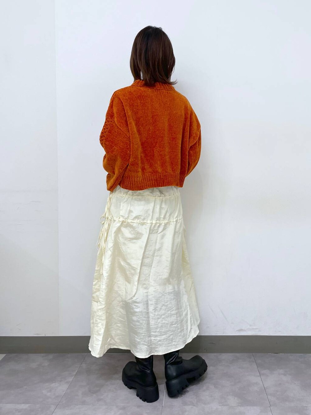 オレンジ系のニット/セーター、ブラック系のブーツ、ホワイト系のスカートを着用したレディースの秋コーディネートの3枚目の写真