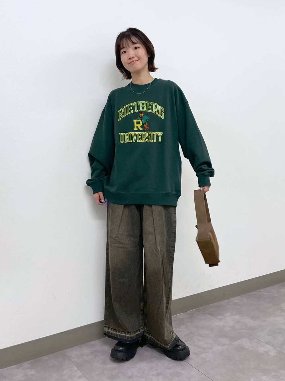 ブラウン系のショルダーバッグ、ブラック系のローファー、グリーン系のスウェットを着用したレディースの冬コーディネートの2枚目の写真