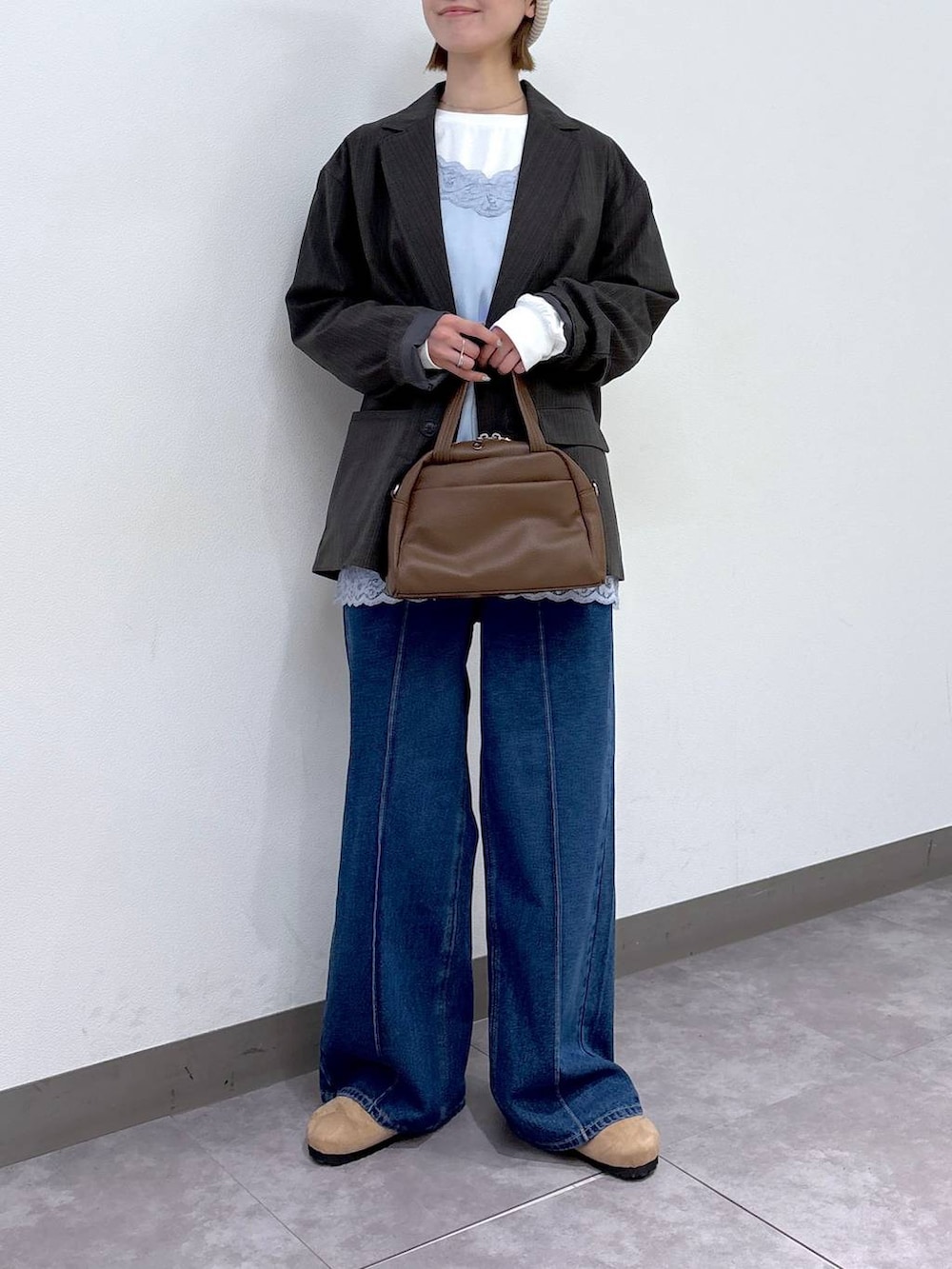 グレー系のテーラードジャケット、ブラウン系のボストンバッグ、ブルー系のデニムパンツを着用したレディースの冬コーディネートの2枚目の写真