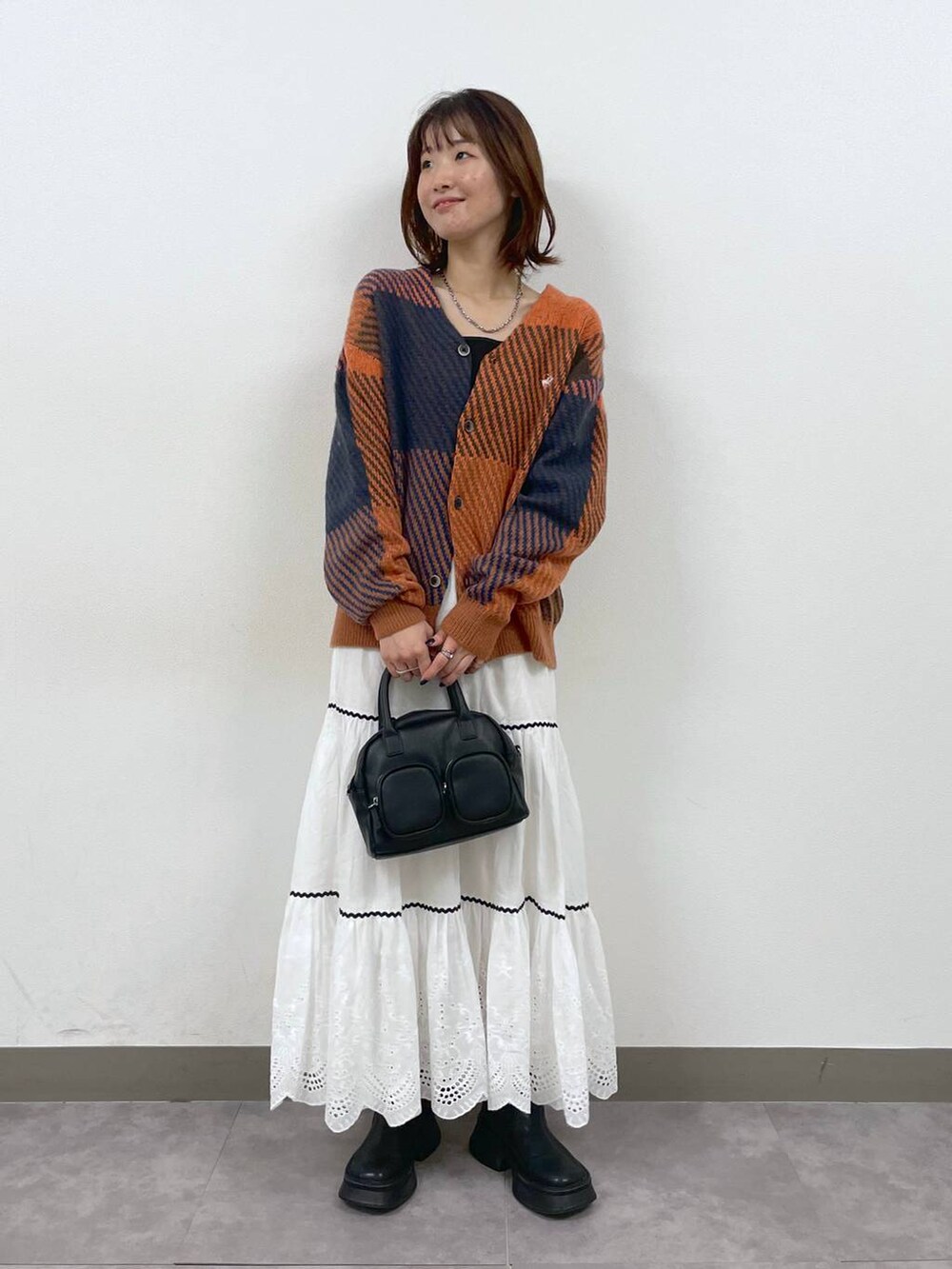 ブラック系のブーツ、ホワイト系のスカート、ブラック系のショルダーバッグを着用したレディースの秋コーディネートの5枚目の写真