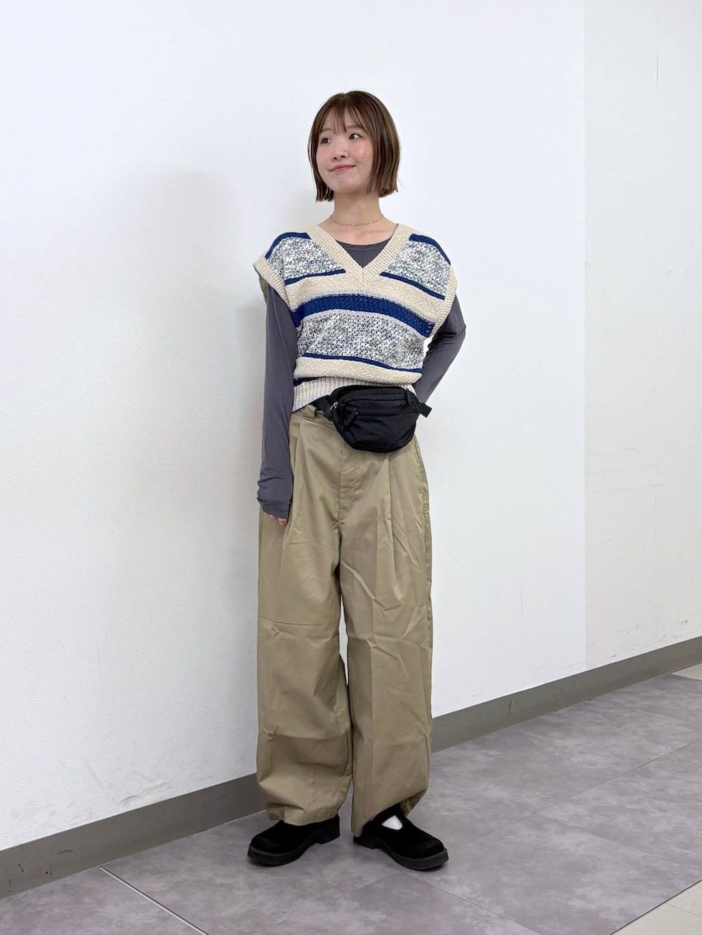 ベージュ系のチノパンツ、ブラック系のボディバッグ/ウエストポーチ、ブルー系のベストを着用したレディースの春コーディネートの3枚目の写真