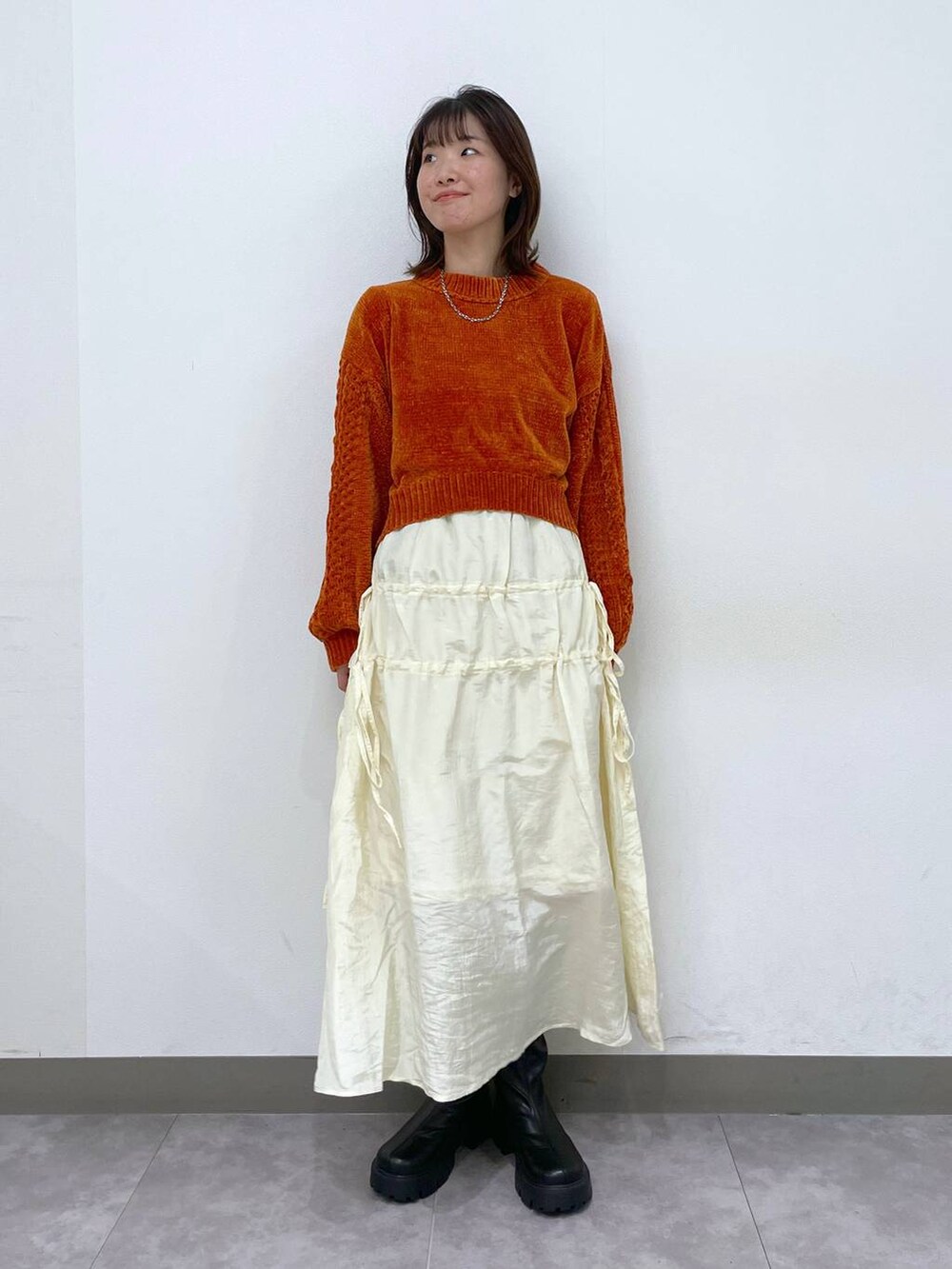 オレンジ系のニット/セーター、ブラック系のブーツ、ホワイト系のスカートを着用したレディースの秋コーディネートの5枚目の写真