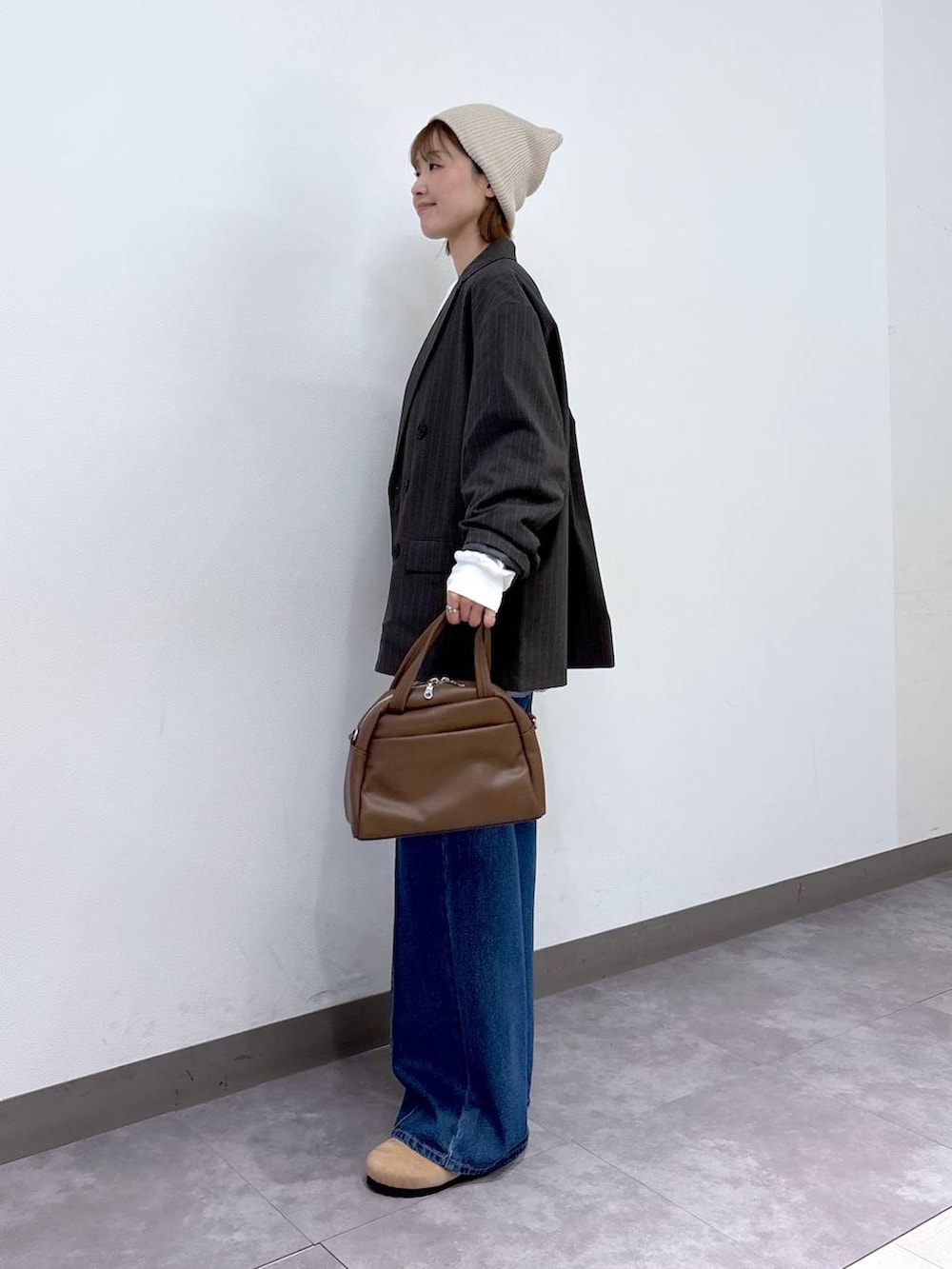 グレー系のテーラードジャケット、ブラウン系のボストンバッグ、ブルー系のデニムパンツを着用したレディースの冬コーディネートの3枚目の写真