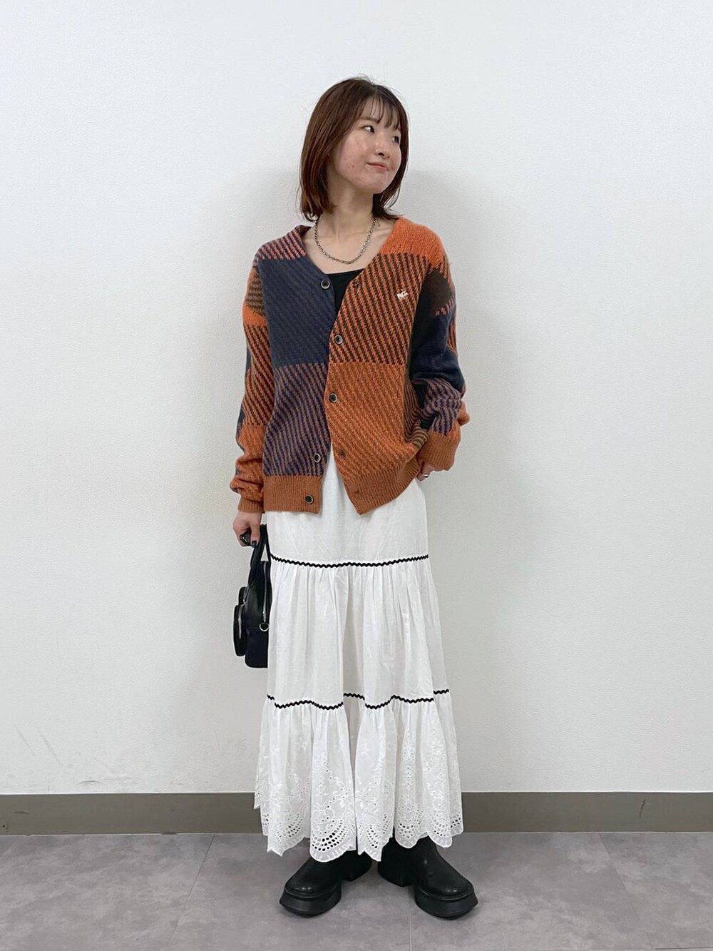 ブラック系のブーツ、ホワイト系のスカート、ブラック系のショルダーバッグを着用したレディースの秋コーディネートの2枚目の写真