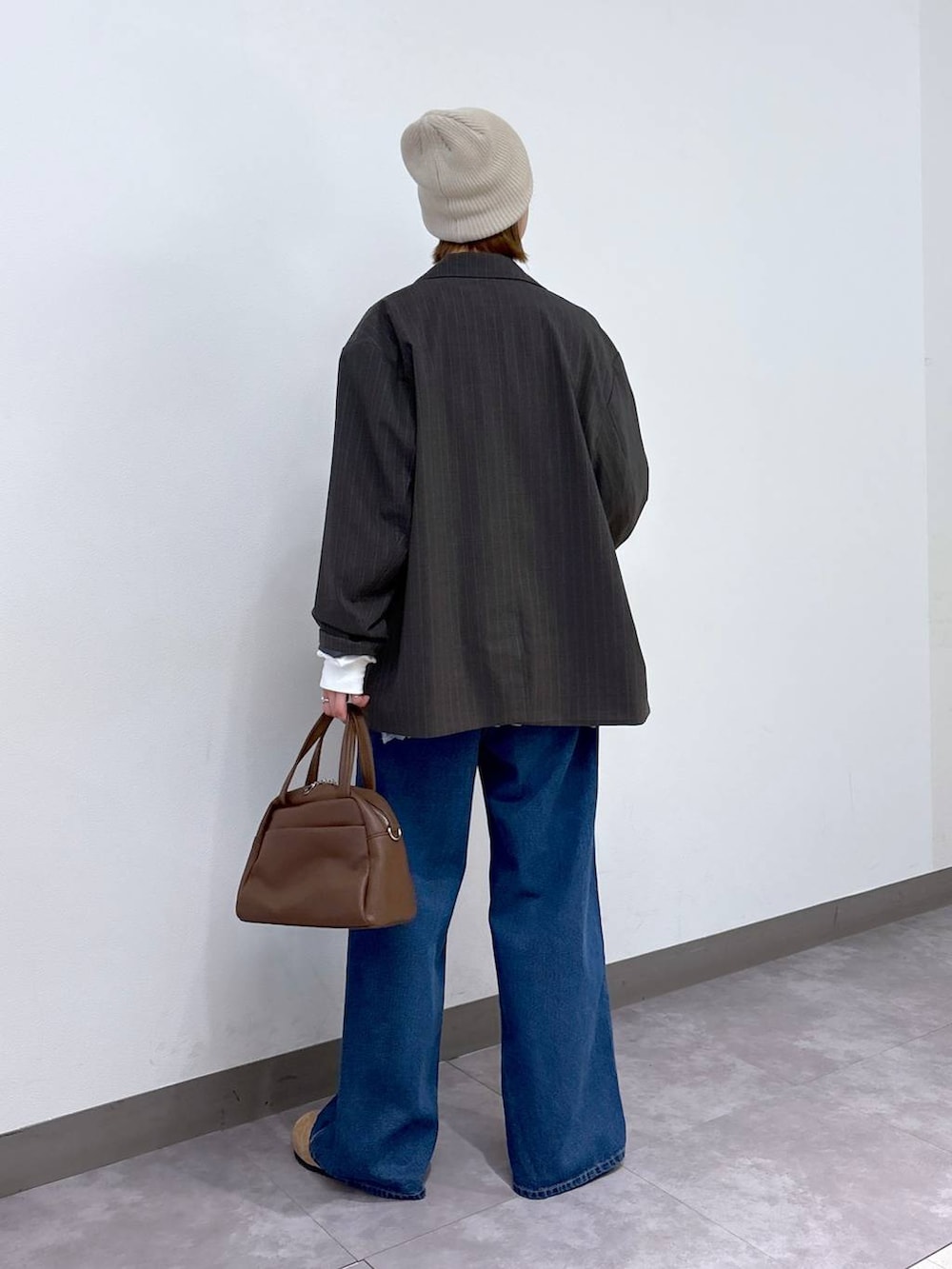 グレー系のテーラードジャケット、ブラウン系のボストンバッグ、ブルー系のデニムパンツを着用したレディースの冬コーディネートの4枚目の写真