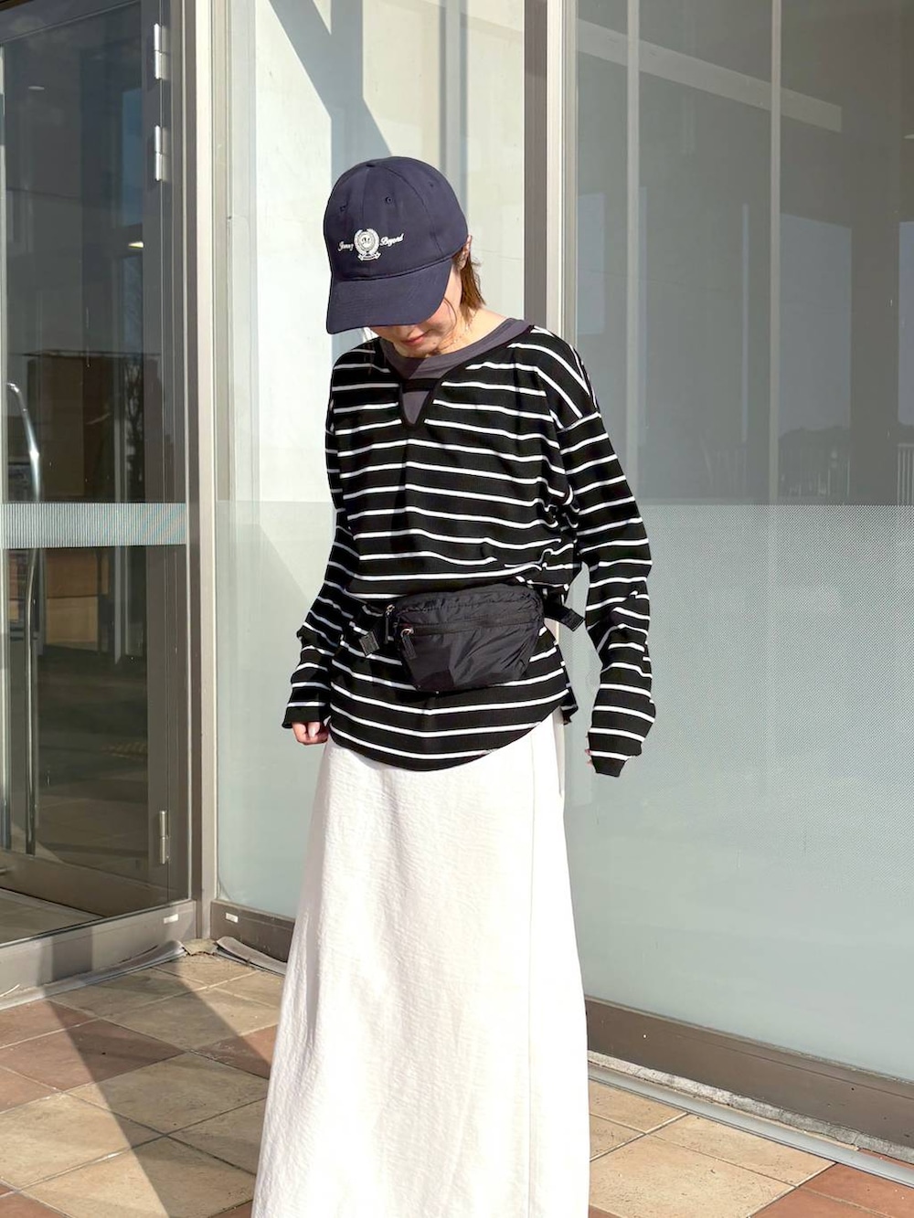 ブラック系のボディバッグ/ウエストポーチ、グレー系のTシャツ/カットソー、ホワイト系のスカートを着用したレディースの春コーディネートの2枚目の写真