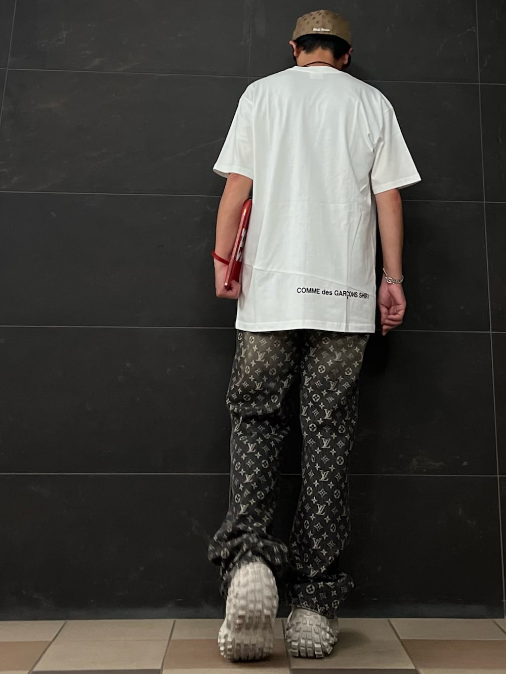 ホワイト系のTシャツ/カットソー、レッド系のクラッチバッグ、ブラック系のデニムパンツを着用したメンズの夏コーディネートの3枚目の写真